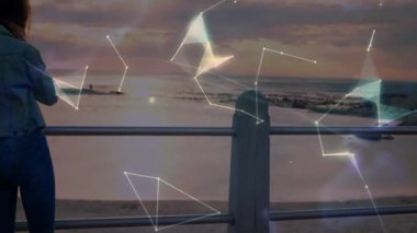 Alacakaranlıkta deniz kenarındaki korkuluklara basan bir kadın ışıldayan veri küresini oluşturan teknoloji hatlarını ateşliyor. Deniz manzarası, tefekkür, fütüristik, dijital ağ, minimalist, sükunet, yenilik