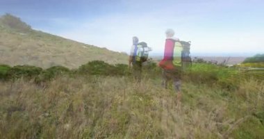 Yürüyüş yapan çift, tarlaları ve okyanusları hayranlıkla seyreden sürülerle tepeye varıyor ve alçalıyorlar. Macera, keşif, manzara, doğa, yolculuk, açık hava, manzara.