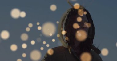 Kukuletalı kadın gökyüzünün altındaki altın kürelerin pazarlamada geri geri gidip kayboluşunu seyrediyor. Sakin, atmosferik, rüya gibi, minimalist, doğa, sükunet, aydınlanma