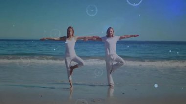 Kadın ve erkek ıslak kumda yürürken, dijital daireler dönerken ağaç pozisyonuna geçiyorlar. Denge, huzur, farkındalık, maneviyat, uyum, refah, meditasyon.