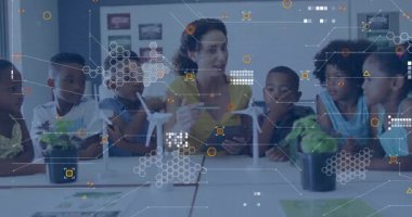 Öğretmen, öğrencileri tablet üzerinde rüzgar enerjisi çizelgeleriyle masa rehberliği yapan türbin modelleri yerleştiriyor. Eğitim, sınıf, yenilenebilir, teknoloji, sürdürülebilirlik, bilim, enerji