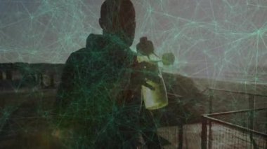 Sahildeki iskelede bir adam şeffaf şişe kaldırıyor ve titreşim teknolojisiyle kırılma oranını analiz ediyor. Deniz manzarası, yenilik, minimalizm, keşif, modern, düşünceli, açık hava.