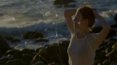 Deniz meltemi saç kaldırma teknolojisi ağı, saçları ayarlayan bir kadının etrafını kaplıyor. Sahil, sükunet, bağlantı, dinginlik, teknoloji, alacakaranlık, doğal
