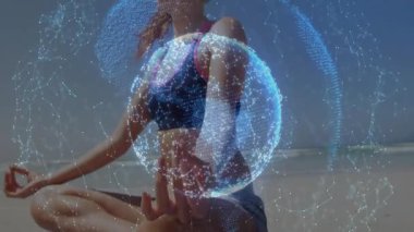 Kumlu kıyıya gelen ve yoga minderini açan bir kadın, meditasyon için dönen veri küresini çağırıyor. Farkındalık, dinginlik, modern, teknoloji, fitness, sağlık, manzara