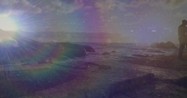 Gün batımı çiftleri, seyahat sahnesinde okyanus dalgalarını kucaklamak ve izlemek için kayalık kıyı şeridine çekiyor. Romantizm, dinginlik, sükunet, doğallık, bağlantı, minimalizm, macera