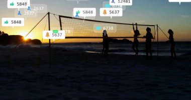 Beş kadın voleybol oynuyor ve alacakaranlık sahilinde toplanıyor sosyal medya uyarı simgelerini su altında bırakıyor. Atletizm, yoldaşlık, günbatımı, siluet, deniz kenarı, aktivite, bilgilendirme