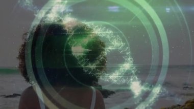 Rocky Beach 'te duran bir kadın sanal halkaları çalıştırıyor, okyanus verilerini sarmal ve kodla analiz ediyor. Fütürist, arayüz, görselleştirme, dijital, sürükleyici, bilim kurgu, teknoloji