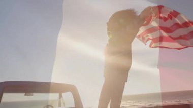 Arka koltuğa adım atan bir kadın seyahat terfisi için mavi üstü açık bir arabanın üzerinde bayrak sallıyor. Vatanseverlik, kutlama, özgürlük, macera, sahil, açık hava, canlı