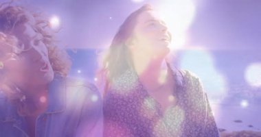 Kadınlar sahilde gülerek ellerinde canlandırılmış ışık örtüsüyle içki reklamı için şişeye giren erkekler olarak gülüyorlar. Arkadaşlar, eğlence, yaşam tarzı, hayat dolu, neşeli, açık hava, arkadaşlık.