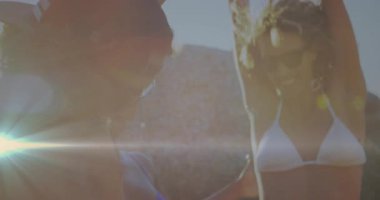 Sahilde dans eden arkadaşlar görünmeyen ritim için bikini giyiyorlar, pazarlama için mercek alevi üretiyorlar. Tatil, yaşam tarzı, enerjik, açık hava, eğlence, canlılık, kutlama