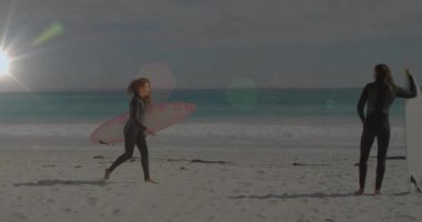 Dişi sörfçü, sörf yapmak için pembe ya da beyaz sörf tahtalarını hizalayarak kumdan kıyıya koşan bir arkadaşını fark ediyor. Sörf, plaj, spor, macera, yaz, etkinlik, doğa