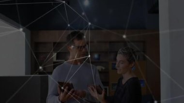 Kadın telefon değiş tokuşu yaparken ve dijital verileri incelerken, adam tablet titreşim ağını dinliyor. İşbirliği, teknoloji, yenilik, profesyonellik, iletişim, dijital, takım çalışması