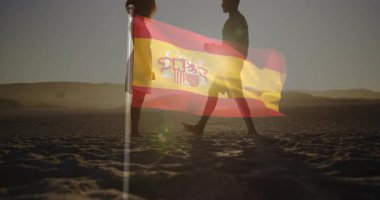 Gün batımında kumulda yürüyen ve İspanyol bayrağı altında evlilik teklifi için diz çöken bir adam. Romantizm, bağlılık, kutlama, manzara, siluet, açık hava, aşk