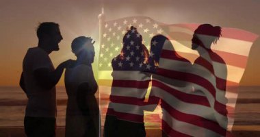 Dostlar gün batımında sahilde yakınlaşır, akıllı telefon kaldırır ve seyahat için bayrak yakalarlar. Siluetler, yoldaşlık, vatanseverlik, boş zaman, sahil, gün batımı, bağlantı