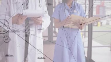 Doktor tıkırdatma tableti ve hemşire dosyaları, tıbbi kayıtların örtüştüğünü gösteren kamera paneli olarak inceliyor. Sağlık, takım çalışması, dijital, profesyonellik, teknoloji, tanı, işbirliği