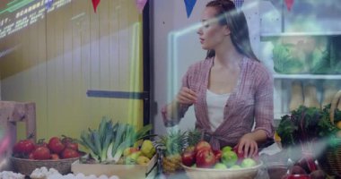 Kadın satıcı sola bakıyor ve domates sepetini işaret ediyor. Perakende satış etiketlerini gösteriyor. Taze ürün, market tezgahı, meyve bahçesi, organik, kırsal, canlı, çiftçi pazarı.