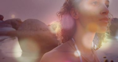 Gün batımında kayalıklardaki kayalara bakan bir kadın tasarım için dans eden Bokeh kürelerini canlandırıyor. Hevesli, dingin, aydınlık, yansıma, soyut, manzara, sükunet