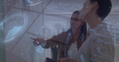 Teknolojiyi etkinleştiren iki iş arkadaşı, verileri analiz eden çizelgelerle etkileşimde bulunuyor. Teknoloji, yenilik, dijital, gelecek, çalışma alanı, işbirliği, görselleştirme