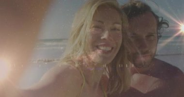 Plajda akıllı telefon yetiştiren bir kadın, çift reklam için gülümserken parlayan mercek yıldız kaplamasını etkinleştiriyor. Romantizm, eğlence, coşku, açık hava, şefkat, mutluluk, huzur.