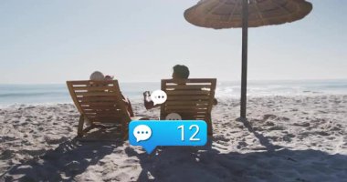 Plaj şemsiyesi altında uzanan pazarlamacı çift, sohbet ikonu olarak tezahürat yaparak uyarıları çarpıyor. Sahil, boş zaman, kutlama, rahatlama, yaşam tarzı, açık hava, tatil