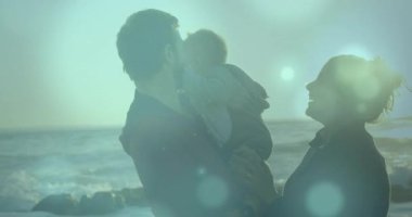 Anne uzanırken, bebek kucağında güneşli bir sahilde çocuğu öpüyor, sağlık inşaatı devam ediyor. Aile, sahil, güneş ışığı, sevgi, bağlantı, sükunet, açık hava