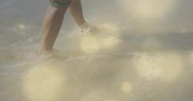 Orta yaşlı bir adam kumda ağırlığını sığ sularda kaydırıyor seyahat ederken ışık yansımalarına neden oluyor. Plaj, ayak sesleri, dalgalar, huzur, parıltı, su, hareket