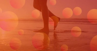 Sağ ayak kaldırma sahile doğru yürüyen kadın, turuncu dairelerin altında seyahat pazarlaması için dalgalanan. Plaj, dinginlik, yansıma, sükunet, ılık renkler, rahatlık, doğa.