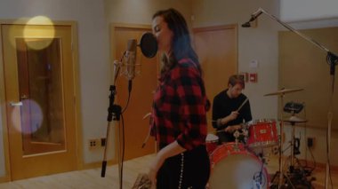 Kadın vokalist mikrofona adım atıyor ve davulcu çalarken yumuşak bir şekilde müzik prodüksiyonu için şarkı söylüyor. Ses, kayıt, performans, akustik, canlı, stüdyo, müzik