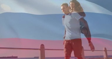 Kadın, erkeğin sırtına tırmanıyor. Bayrak ile sevgiyi paylaşıyor. Seyahat için el sallıyor. Romantik, boş zaman, arkadaşlık, açık hava, yaz zamanı, neşeli, manzaralı