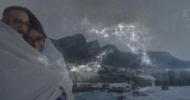 Kayalık kıyılarda ortaya çıkan bir çift battaniyeye sarılı haldeyken, nebula alevleri medyanın üzerinde sürükleniyor. Romantik, kıyı, gece gökyüzü, gökyüzü, samimiyet, dinginlik, vahşi doğa.