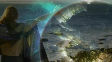 Kayalık kıyı şeridinde kollarını kaldıran şallı bir kadın parlayan teknoloji küresi yaratıyor ve dünyayı haritalıyor. Kozmik, mistik, manzara, ortam, fantezi, ruhani, yenilik