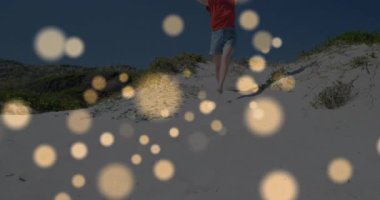 Kum tepeciğine basan bir kadın inişe geçiyor altın bokeh ışıklarıyla koşuyor. Macera, eğlence, oyun, açık hava, hayat dolu, tasasız, yaşam tarzı