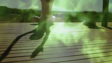 Güvertede oturan bir kadın sağlıklı olmak için kollarını kaldırıyor, dönen yeşil enerji sisi yaratıyor. Meditasyon, rahatlama, dinginlik, doğa, mistik, sükunet, denge