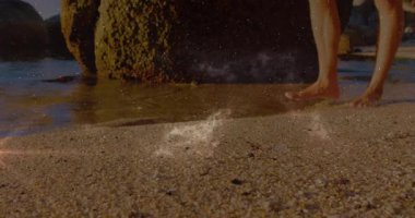 Kıyı şeridine çıplak ayaklı bir adamın girdiği ve parlak merceğin kayayı geçtiği bir seyahat klipsi. Sahil, sahil, ayak izleri, su, sprey, yosun, manzara