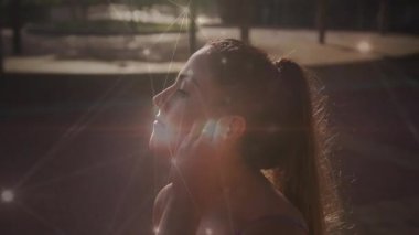 Kablolu kulaklığı kulağına çeken bir kadın, dış sahada ses için ağ örtüsü ile uyum sağlıyor. Atletik, teknoloji, doğa, fitness, dijital, aktif giyim, kentsel