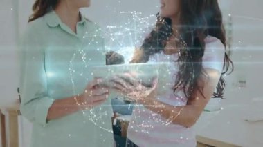 Elinde tablet olan iki kadın iş verilerini tartışırken ekranda hareketli küre titreşimi yaratıyor. İşbirliği, takım çalışması, dijital, yenilik, ağ oluşturma, modern, profesyonel