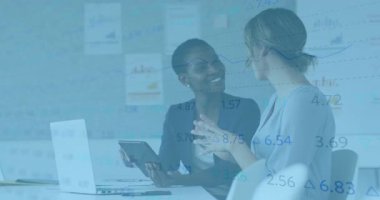 İki kadın tableti paylaşırken finans incelemesine başlıyor, biri bilgisayarında grafikle yazı yazıyor. İşbirliği, takım çalışması, modern, kurumsal, tartışma, analiz, teknoloji