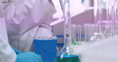 Kadın bilim adamı laboratuvar bankından mikropipet alıyor, örnek alıyor ve rafa koyuyor. Laboratuvar, araştırma, bilim, kesinlik, enstrümantasyon, saflık, deney