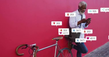 Kırmızı duvara yaslanmış bir adam telefonun kilidini açıyor ve bisiklet etrafında süzülen sosyal uyarılar veriyor. Kentsel, modern, canlı, iletişim, bağlantı, gündelik, sokak