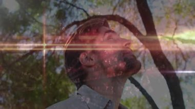 Adam tepe örtüsünün altında dikiliyor, başını arkaya eğiyor ve ağaçların tepelerini gösteren teknolojik rakamlar beliriyor ve azalıyor. Doğa, teknoloji, dijital, dingin, fütüristik, aydınlanma, yenilik