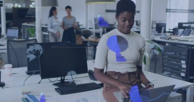 Krem rengi bluzlu ve kahverengi etekli bir kadın açık planlı ofiste dizüstü bilgisayarda monitörlerle yazı yazıyor. İşbirliği, üretkenlik, modern, profesyonel, çalışma alanı, takım çalışması, iş dünyası