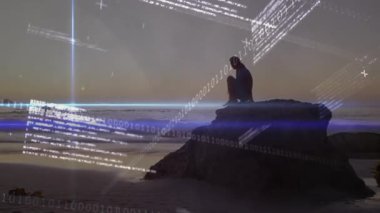 Kayalık kayalıklara yaklaşan, telefonları çeken, okyanus üzerinde parlayan teknolojiyi kullanan bir kadın. Doğa, manzara, günbatımı, huzur, bağlantı, teknoloji, ilham