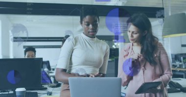 Krem rengi bluz ve pembe bluz giyen iki iş arkadaşı bilgisayardaki verileri tabletle tartışıyor. İşbirliği, takım çalışması, modernlik, teknoloji, profesyonel, üretkenlik, yenilik