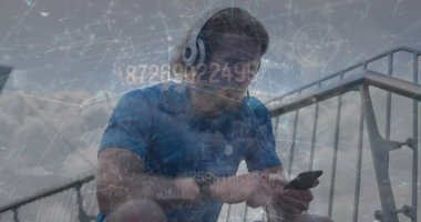 Oturan atletik adam tribünlerdeki akıllı telefonlara odaklanıyor, kulaklıkları ve spor saatleriyle. Teknoloji, fitness, açık hava, atletizm, fütürizm, aktif giyim, dijital