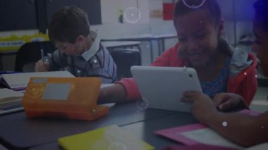 Sınıf arkadaşları not yazıyor, tablete dokunuyor ve teknolojik görüntüler aktive edilirken izliyorlar. Öğrenciler, eğitim, dijital öğrenim, işbirliği, sınıf, yenilik, yaratıcılık