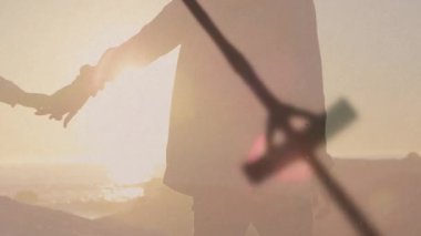 Haç kolyesini gösteren bir klip. Çerçeve kayan odak çiftine sallanıyor. Sahilde yürüyen günbatımı. Romantik, siluet, günbatımı, okyanus, sükunet, mücevher, sükunet