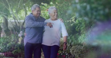 Yaşlı çiftler bahçe yolunda yürüyor, adam çalılara doğru hareket ediyor, sağlık için yaprak simgelerini aktifleştiriyor. Romantik, dostluk, sükunet, doğa, rahatlık, sağIık, resim gibi.