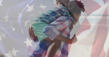 Diz çöken ve oğlunu sırtında taşıyarak yürüyen bir bayrak taşıyan bir kadın. Ebeveynlik, açık hava, eğlence, bağlantı, mutluluk, destek, aile bağı