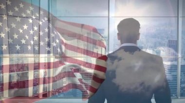 Pencerenin önünde duran bir iş adamı, bulutlarla birlikte Amerikan bayrağının hareketlenmesine neden oluyor. Şirket, vatanseverlik, gökdelen, yansıma, modern, hırs, liderlik
