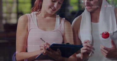 Panoya metrik yazan bir kadın ve performans ölçümlerini güncelleyen bir spor salonu çizelgesi olan stajyer. Fitness, performans, analitik, eğitim, veri, sağlık, motivasyon